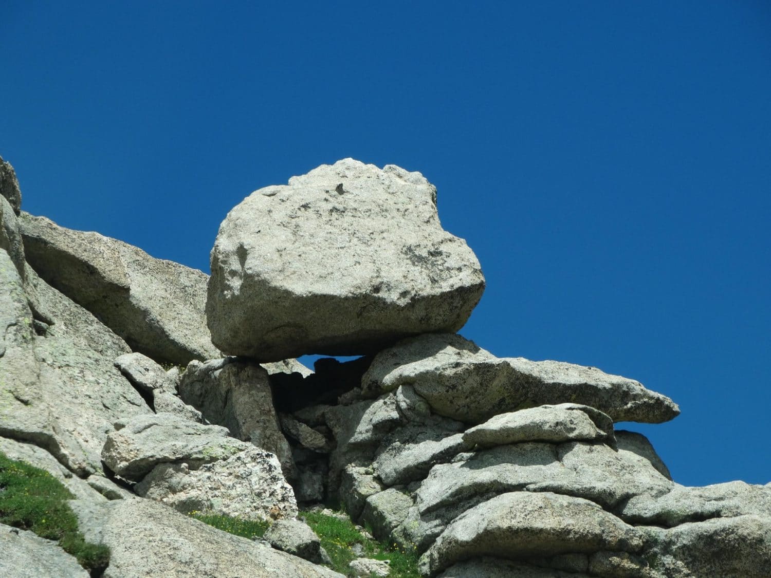 bolder perched on the side of a hill. Blue sky in the background.